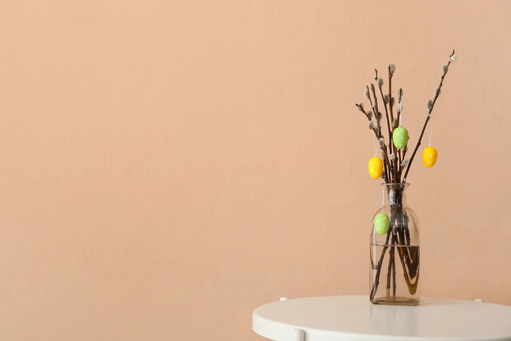 vase with willow branches and painted easter eggs on table near beige wall photo 1